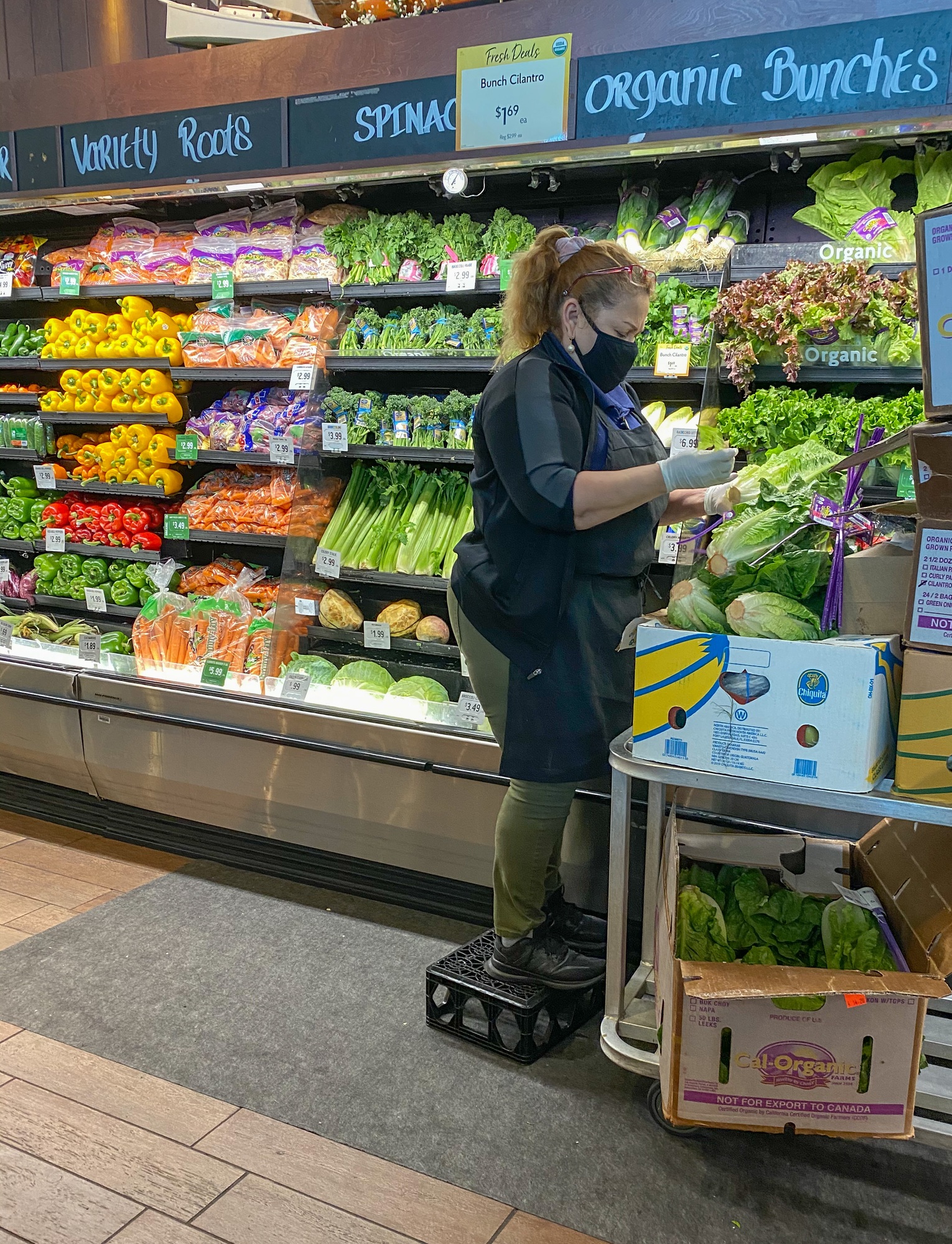 A woman working at a grocery store restocking food in gloves and a mask